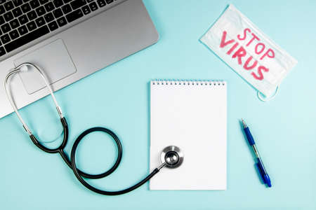 Flatlay doctor workplace with laptop, mask and notepad mock up. Text on medical mask "stop virus"の写真素材