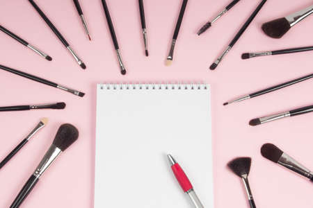 Large set of makeup brushes with a notebook and pen mock-up on a pink background. Flat layの写真素材