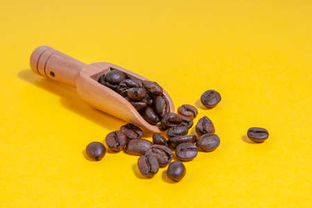 Coffee beans in a coffee spoon scattered on yellow background.の写真素材