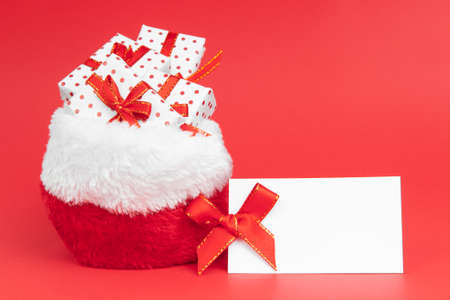 Heaps of christmas gifts in Santa Claus sack wrapped in gift paper polka with festive ribbon on red background with note mock up.の写真素材