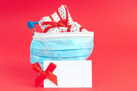Shopping trolley with gifts in a protective face mask on a red background with note mock up. The concept of buying gifts for the holiday during the virus.の写真素材