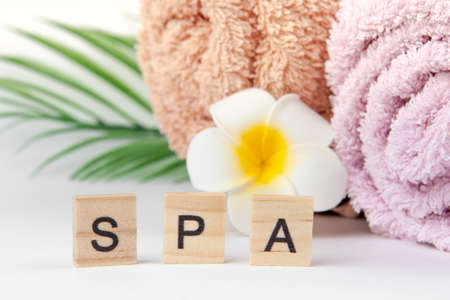 Pastel towels with Plumeria flowers with tropical palm leaves and inscription "SPA" on light background with copy space. Skin care and spa concept.の写真素材