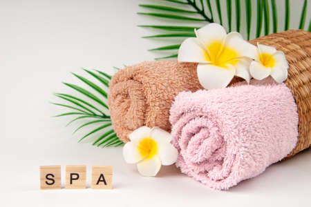Pastel towels with Plumeria flowers with tropical palm leaves and inscription "SPA" on wooden cubeの写真素材