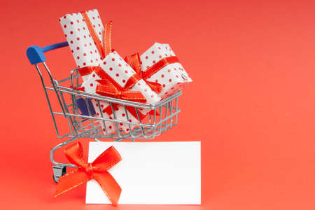 Trolley full of gifts on a red background with mock up and copy space. Concept for christmas, holidays, discounts and shopping.の写真素材