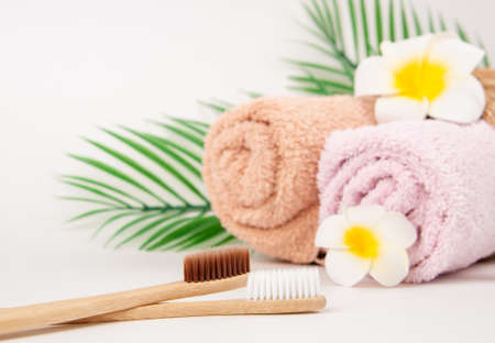 Bamboo toothbrushes with towels in a wicker wooden basket and palm leaves and plumeria flower with copy space on white background. Spa, healthy lifestyle and ecology concept.の写真素材