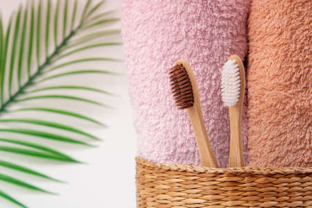 Bamboo toothbrushes with towels in a wicker wooden basket and palm leaves with copy space on white background. Spa, healthy lifestyle and ecology concept.の写真素材