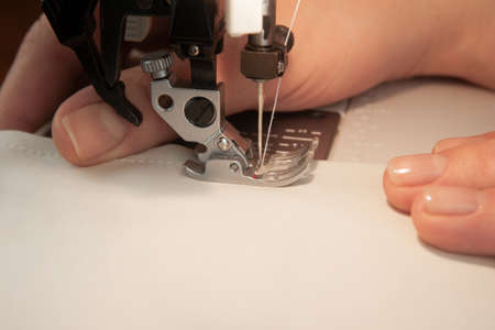 Female hands hem white fabric on a sewing machine with place for text. Atelier and handicraft concept.の写真素材