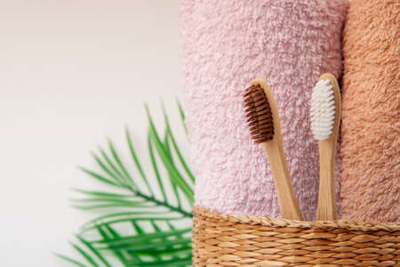 Bamboo toothbrushes with towels in a wicker wooden basket and palm leaves with copy space on white background. Spa, healthy lifestyle and ecology concept.の写真素材