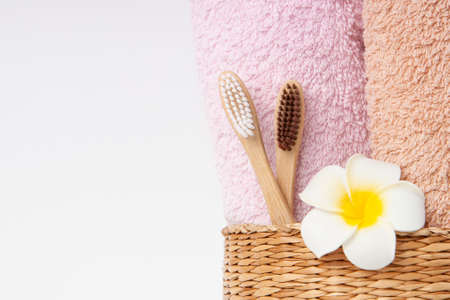 Bamboo toothbrushes with towels in a wicker wooden basket and plumeria flower with copy space on white background. Spa, healthy lifestyle and ecology concept.の写真素材