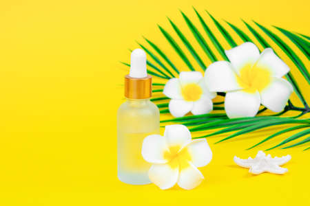 Cosmetic oil in dropper bottle with plumeria flowers with palm leaves on yellow background with place for text.の写真素材