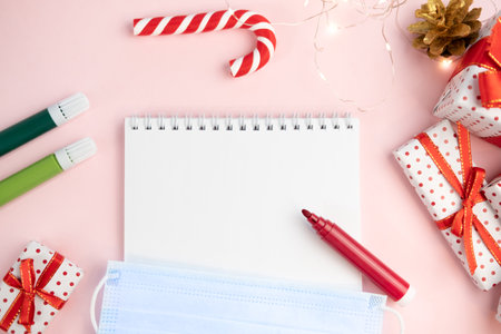 Notepad wish list on a pink table with felt-tip pens with protective face mask on a Christmas background with mock up. Concept of christmas, new year, plans and making wishes and corona virusの写真素材