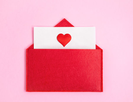 Red open envelope with a sheet of paper with a heart on a pink background with copyspace. Valentine's day holidays concept and love notesの写真素材