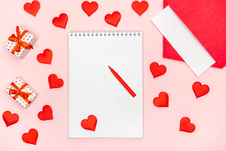 Flatlay notepad mock up with felt-tip pen with a red envelope with hearts and gifts on a pink background. Concept of valentine's day and writing love lettersの写真素材