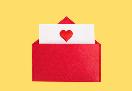 Red open envelope with a sheet of paper with a heart on a yellow background with copyspace. Valentine's day holidays concept and love notes, christmas and new year letters for Santa Clausの写真素材