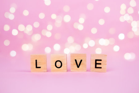 Words Love on a blurred pink background with a beautiful bokeh from a gold garland and lights. Place for the text, copyspace. Concept of holidays valentines day, mothers day, fathers day and romanceの写真素材