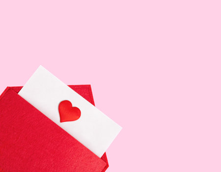 Red open envelope with a sheet of paper with a heart on a pink background with copyspace. Valentines day holidays concept and love notes, christmas and new year letters for Santa Clausの写真素材