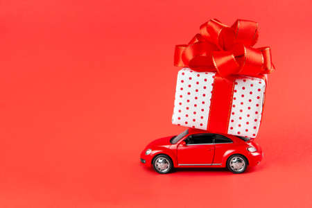 Moscow, Russia, January 14, 2021. Red retro car makes delivery for the holidays on March 8, Valentines Day, February 14, Christmas, New Year. Toy car with gift on a red background.の写真素材