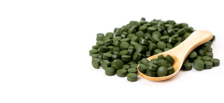 Banner spirulina algae tablets with a wooden spoon isolated on white background. Nutritional supplements, vitamins and health concept.の写真素材