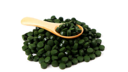 Spirulina algae tablets with a wooden spoon isolated on white background. Nutritional supplements, vitamins and health conceptの写真素材