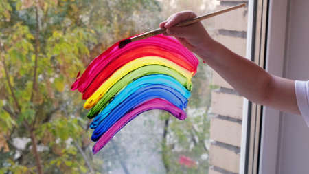 Kid hand painting colorful rainbow on window during 
 quarantine at home. Stay at home due to danger oの写真素材