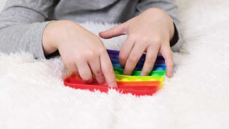 Little boys hands are playing an educational game. Colorful antistress sensory toy fidget push pop in toddlers hands. Antistress trendy pop toy. Rainbow sensory fidget. New trendy silicone toyの写真素材