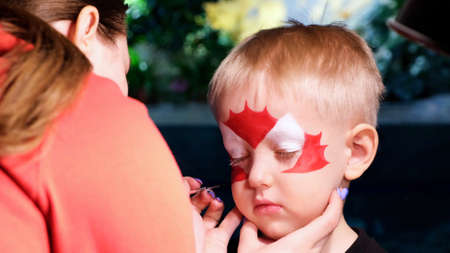 A little boy is put face painting on his face, his face is painted with paint. The concept of childrens holiday, childhood, entertainment event, Halloweenの写真素材