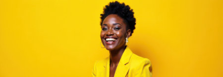 Studio portrait of a cheerful young african american businesswoman wearing a yellow suit, smiling brightly against a vibrant yellow backdrop, perfect for banners and promotional materialの素材