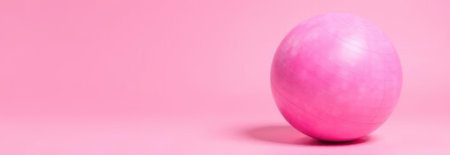 Pink fitness ball on a pink background providing ample copy space, ideal for fitness, wellness or banner designsの素材
