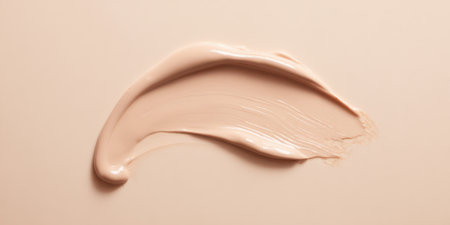 Smooth beige foundation cream creating a textured smear on a matching background, representing skincare, make-up, and beauty product swatches for cosmetic advertisingの素材