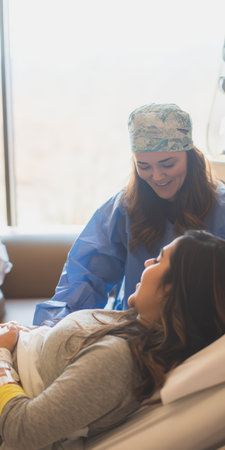 Healthcare professional wearing scrubs and a surgical cap interacting with a woman lying in a hospital bed, offering comfort and support during recoveryの素材