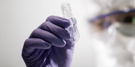 Scientist in a protective hazmat suit and purple medical gloves holding a test tube with liquid, performing laboratory research for vaccine development and disease preventionの素材