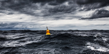 Yellow navigation buoy marking a safe passage and warning boats about dangers in the dark rough ocean under a dramatic, cloudy, and stormy sky, symbolizing solitude and resilienceの素材