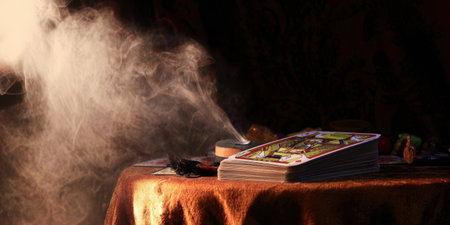 Tarot cards stacked on a table with a feather and burning incense creating an ethereal smoke, representing spirituality, divination, and fortune-telling in a mystical settingの素材