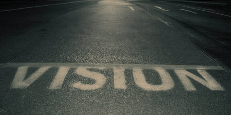 Vision word painted white on a dark asphalt road surface, representing future goals, new directions, inspiration, and strategic planning, with dim light illuminating the path aheadの素材