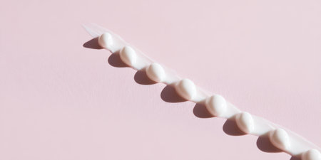 White cosmetic cream blobs are smoothly swatched forming a diagonal line on a soft pink surface, creating elegant shadows and highlighting the product's textureの素材