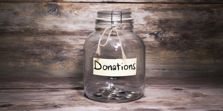 Glass jar labeled donations collecting coins on a rustic wooden surface, symbolizing fundraising, charity and community support for nonprofit causes and financial assistance effortsの素材