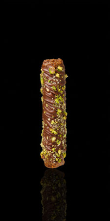 Vertical chocolate dessert bar topped with chopped pistachios, glossy coating and subtle reflection on a dark backgroundの素材