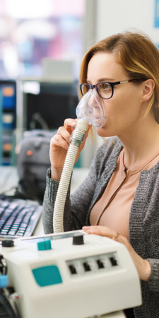 Woman wearing a face mask attached to a spirometer machine, undergoing a pulmonary function test for respiratory health examination in a medical clinicの素材