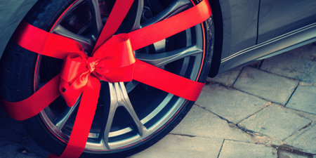 Modern automobile wheel celebrating a special occasion with a vibrant red ribbon and festive bow, representing a present, surprise, or promotional offeringの素材