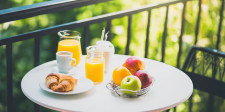 Refreshing balcony breakfast with croissants, coffee, orange juice and a bowl of fresh fruit on a white table bathed in warm sunlight, perfect for a summer getawayの素材