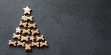 Dog treats and bone-shaped cookies are arranged into a festive christmas tree shape, featuring star-dusted biscuits on a dark background, representing pet holiday cheer and seasonal momentsの素材