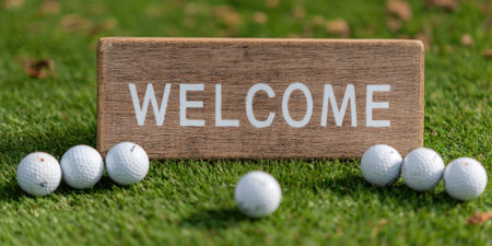 Wooden welcome sign on bright green grass framed by white golf balls, inviting players to a golf course event or tee-off; sunny outdoor greeting for leisure and sportの素材