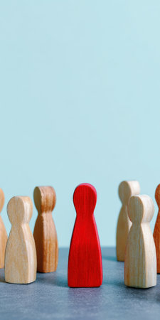 Red wooden figure standing prominently among many other natural colored figures, depicting concepts of leadership, individuality, and uniqueness within a group or teamの素材