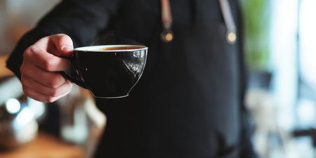 Barista wearing a black apron presenting a steamy cup of hot coffee, symbolizing hospitality, excellent service, and a welcoming cafe experience for customersの素材