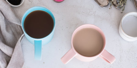 Two pastel mugs, one blue and one pink, filled with hot coffee and a milky drink, placed on a light concrete countertop, creating a cozy and inviting flat lay sceneの素材