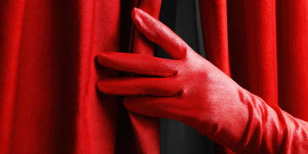 Red gloved hand gently pulling back a lush velvet theater curtain, revealing a glimpse of the hidden stage or secret beyond, embodying mystery, anticipation, and performanceの素材