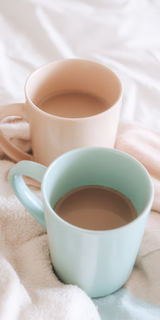Two pastel ceramic mugs filled with warm coffee or tea resting on soft bedding, creating a cozy and relaxing atmosphere perfect for a comfortable morning or slow livingの素材