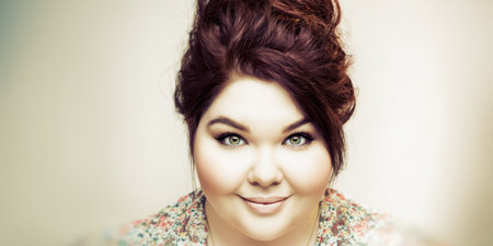 Plus size woman with brown updo and green eyes smiling confidently at camera, radiant headshot conveying body positive self-acceptance, authenticity and joyful empowermentの素材