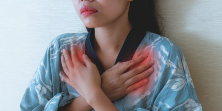 Woman feeling severe chest pain and heart discomfort, indicating a potential heart attack or other cardiac condition, holding her chest with a pained expressionの素材