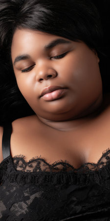 Plus-size black woman in black lace lingerie with eyes closed, serene and confident, embracing self-love, body positivity and peaceful relaxation in an intimate studio portraitの素材